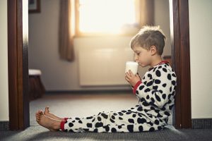 Little boy wearing pyjamas drinking glass of milk in morning